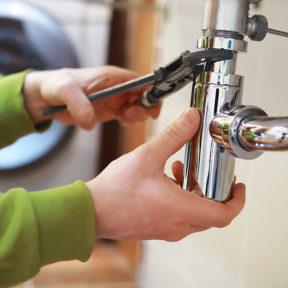 Plumber tightening a chrome sink trap with a wrench